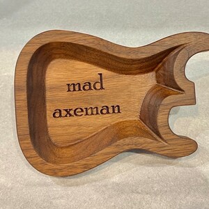 May include: A wooden guitar-shaped trinket tray with the words "mad axeman" engraved on the surface.