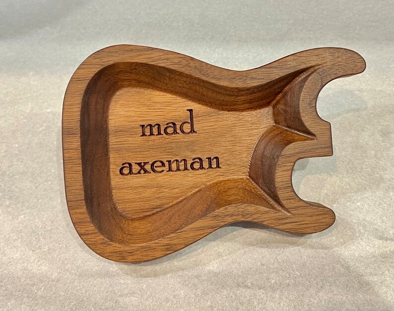 May include: A wooden guitar-shaped trinket tray with the words "mad axeman" engraved on the surface.