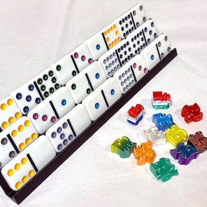 May include: A set of white dominoes with colored dots, arranged in a brown tray. Various colorful game pieces are scattered nearby. The dominoes have dots in blue, green, purple, and yellow. A classic game set.