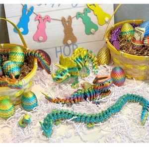 Peut inclure: Une collection d'&oelig;ufs de P&acirc;ques iris&eacute;s dans un panier en osier jaune. Les &oelig;ufs sont d&eacute;cor&eacute;s d'un dragon, d'un dinosaure et d'autres motifs color&eacute;s. Le panier est entour&eacute; de papier blanc d&eacute;chiquet&eacute; et d'une pancarte qui dit "HOP".