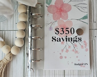 May include: Clear binder with a floral design and the text "$350 Savings." The design features pink flowers and green leaves. A wooden bead garland and a white flower are in the background.