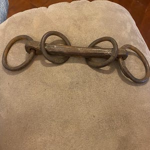 May include: A rustic, hand-forged metal chain with multiple interlocking rings. The chain is made of dark brown metal and has a rough, textured surface.