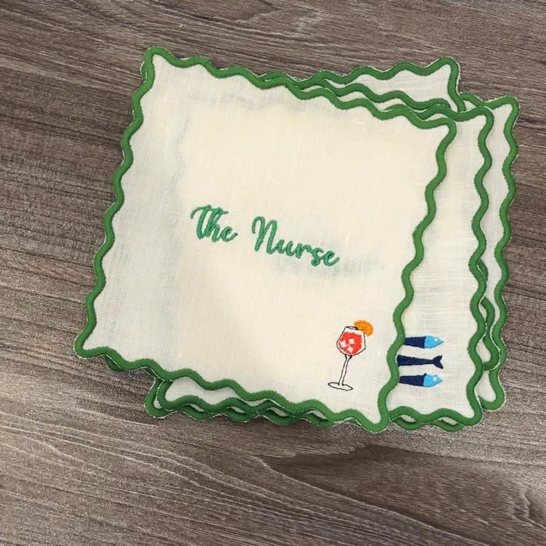 May include: White handkerchiefs with green scalloped edges. The text "The Nurse" is embroidered in green. A cocktail glass and three blue fish are also embroidered on the handkerchief.
