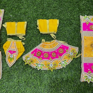 Puede incluir: Un conjunto de ropa de tela amarilla y rosa con bordados y adornos intrincados. El conjunto incluye una falda, una blusa, pantalones y una diadema.