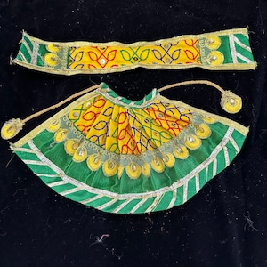 May include: A green and yellow skirt with gold trim and embellishments. The skirt is made of fabric with a geometric pattern. It is a traditional Indian garment.