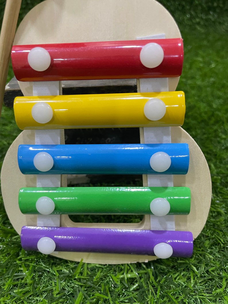 May include: A wooden xylophone toy with five colourful bars: red, yellow, blue, green, and purple. Each bar has two white plastic knobs on the ends.