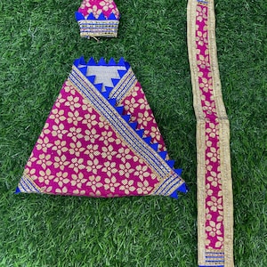 May include: A pink fabric with a gold floral pattern and blue trim. The fabric is folded into a triangle shape and is accompanied by a matching hat and a long sash.