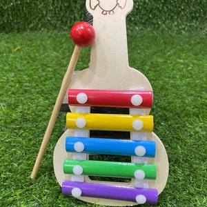 May include: A wooden xylophone shaped like an owl with a red mallet. The xylophone has five bars in rainbow colours: red, yellow, blue, green, and purple.