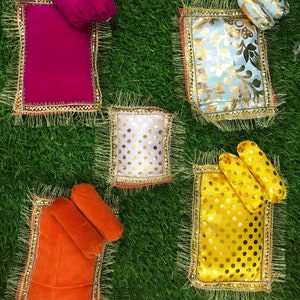 Puede incluir: Cuatro camas decorativas con almohadas, cada una con un color y un patrón diferente. Las camas están hechas de tela y tienen ribetes dorados. Las camas están sobre una superficie de hierba verde.