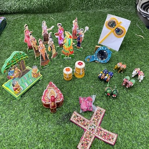 Puede incluir: Una colección de figuritas de madera de colores, que incluye un grupo de personas, un árbol y animales. También hay varios artículos decorativos, como un espejo, una pluma de pavo real y una pequeña caja. Los artículos están dispuestos sobre una superficie de césped artificial verde.