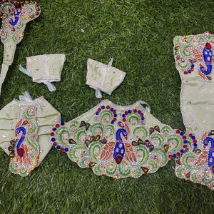 May include: A set of light green fabric clothing with peacock embroidery and embellishments. The set includes a top, two sleeves, a headpiece, and a pair of trousers.