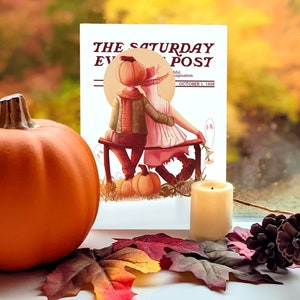 May include: An orange pumpkin sits next to a vintage magazine cover with the text "The Saturday Evening Post." The cover art depicts two figures with pumpkin heads on a bench. A lit candle, fall leaves, and a pinecone complete the autumn scene.