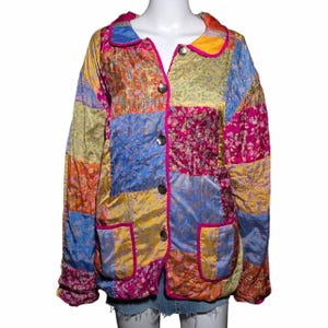Puede incluir: Una chaqueta acolchada de manga larga con un diseño de patchwork vibrante que presenta varios estampados florales y de cachemira en tonos amarillo, azul, naranja y magenta. La chaqueta tiene cuello redondo, cuatro botones y dos bolsillos.
