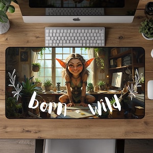 Puede incluir: Alfombrilla de escritorio rectangular con una ilustración de un personaje sonriente parecido a un elfo con grandes orejas, sentado en una habitación. La alfombrilla tiene las palabras "born wild" en escritura blanca. La alfombrilla está rodeada de plantas y material de oficina.