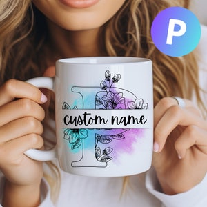 Può includere: Una tazza in ceramica bianca con un contorno nero della lettera "P" e disegni floreali. La tazza ha uno sfondo ad acquerello in tonalità di blu e viola. Il testo "custom name" è stampato su uno striscione nero attraverso la tazza.
