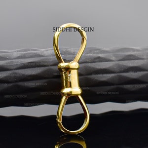 May include: A gold-coloured metal clasp with two loops. The clasp is designed to connect two pieces of jewellery or other items.