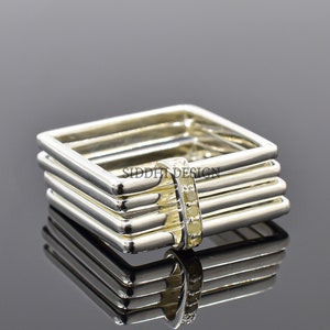 May include: A silver square ring with multiple bands and a row of small clear stones in the centre.