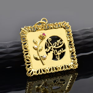 May include: Gold pendant with a square frame and a cutout design of a rose and the words "Love You". The rose has a red center and white pearl accents.