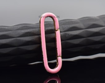 May include: A pink enamel oval-shaped clasp with gold-colored accents. The clasp is shown against a dark, textured background. The text "SIDDHI DESGIN" is visible on the clasp.