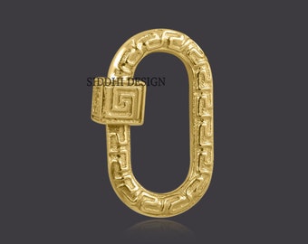 May include: Gold-toned metal clasp with a Greek key design. The clasp is oval-shaped and has a square-shaped piece on one side.