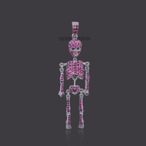Puede incluir: Colgante de esqueleto plateado con calavera y caja torácica adornada con piedras preciosas rosas. El colgante tiene un lazo para una cadena. El texto "SIDDHI DESIGN" es visible en la imagen.