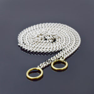 Puede incluir: Collar de cadena de plata con dos anillos de oro en el extremo. La cadena está enrollada y los anillos son visibles. El texto "SIDDHI DESIGN" es visible en la cadena.