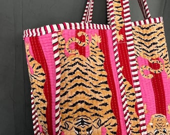 Könnte beinhalten: Eine rosa und rote gestreifte Tragetasche mit gestepptem Design, das ein sich wiederholendes Muster von Tigern zeigt. Die Tasche hat zwei lange Henkel mit weißen Streifen.