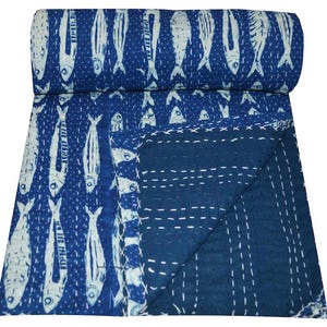 May include: A blue kantha quilt with a white fish pattern. The quilt is folded in half and the back side is a solid blue color.