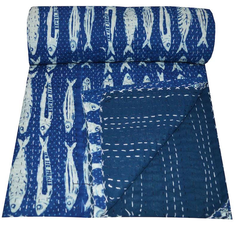 May include: A blue kantha quilt with a white fish pattern. The quilt is folded in half and the back side is a solid blue color.