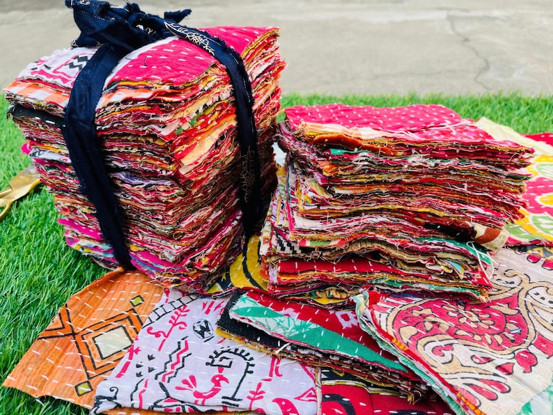 K&ouml;nnte beinhalten: Ein Stapel bunter Stoffquadrate, die mit einem schwarzen Band zusammengebunden sind. Die Stoffquadrate bestehen aus verschiedenen Materialien und Mustern, darunter Blumen, geometrische Muster und Paisley. Die Quadrate sind in zuf&auml;lliger Reihenfolge angeordnet und bilden so ein optisch ansprechendes und strukturiertes Display.