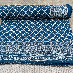 Peut inclure: Une courtepointe kantha bleue et blanche avec une bordure paisley et un motif d'écailles qui se chevauchent. La courtepointe est pliée en deux et repose sur une surface gris clair.