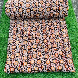 May include: A black fabric with a floral pattern in shades of orange, white, and red. The fabric is rolled up and lying on a green surface.