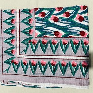 May include: A gray and white quilted throw blanket with a floral pattern of pink and red tulips. The blanket has a border of green leaves and a white background.