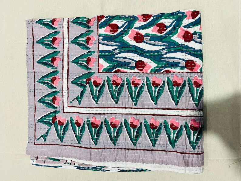 May include: A gray and white quilted throw blanket with a floral pattern of pink and red tulips. The blanket has a border of green leaves and a white background.