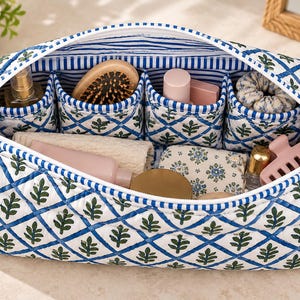 May include: A quilted fabric toiletry bag featuring a white base with a blue diamond grid pattern and green leaf motifs. The interior is lined with blue and white stripes and contains four open pockets holding various personal care items.