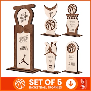 Puede incluir: Conjunto de 5 trofeos de baloncesto de madera. Los trofeos presentan diseños de baloncesto, siluetas de jugadores y texto como "Best Player 202X" y "Basketball Cup".
