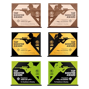 Puede incluir: Una colección de placas "Top Shooter Award" en varios diseños. Algunas son de madera con siluetas cortadas con láser de una persona apuntando con un rifle. Otras presentan fondos negros, dorados y verdes con el texto y el logotipo del premio.