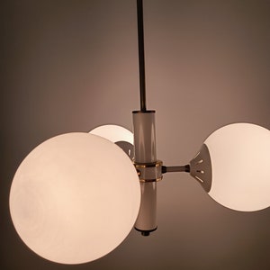 Peut inclure: Un lustre moderne avec trois abat-jours sph&eacute;riques en verre d&eacute;poli. Le luminaire a une finition blanche et dor&eacute;e avec une tige centrale et des bras s'&eacute;tendant pour tenir les globes. Le lustre est suspendu au plafond.