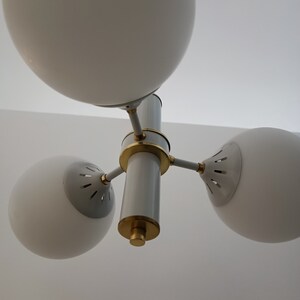 Peut inclure: Un lustre moderne blanc et dor&eacute; avec trois abat-jours sph&eacute;riques en verre. Le luminaire poss&egrave;de une colonne centrale avec des accents dor&eacute;s et trois bras pour soutenir les abat-jours. Con&ccedil;u pour un montage au plafond.