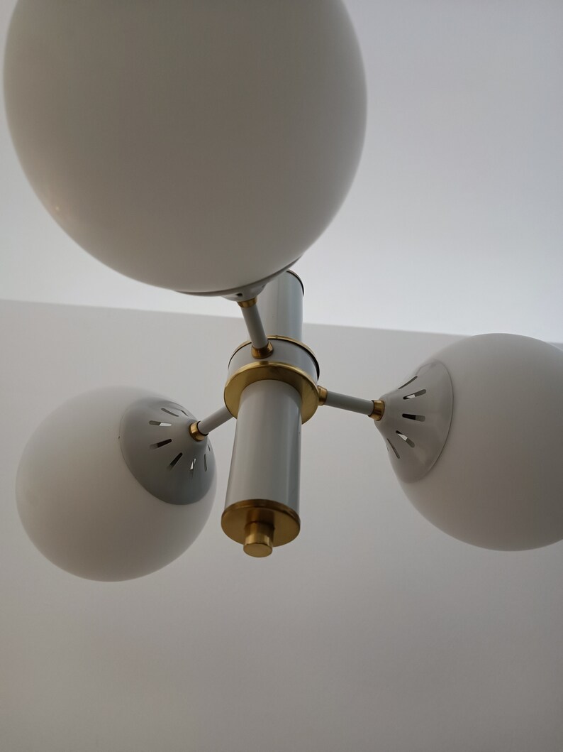 Peut inclure: Un lustre moderne blanc et dor&eacute; avec trois abat-jours sph&eacute;riques en verre. Le luminaire poss&egrave;de une colonne centrale avec des accents dor&eacute;s et trois bras pour soutenir les abat-jours. Con&ccedil;u pour un montage au plafond.