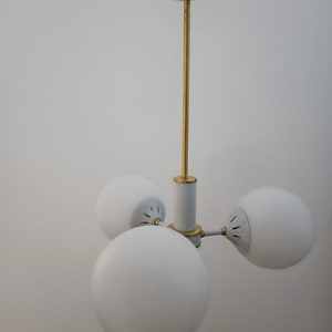 Peut inclure: Un plafonnier moderne avec trois abat-jours sph&eacute;riques en verre blanc. Le luminaire a une tige et des accents dor&eacute;s, avec un corps central blanc et dor&eacute;. La lumi&egrave;re est con&ccedil;ue pour &ecirc;tre mont&eacute;e au plafond.