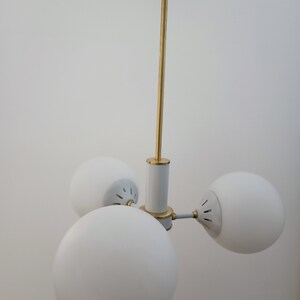 Peut inclure: Un plafonnier moderne avec trois abat-jours globulaires blancs. Le luminaire pr&eacute;sente une tige centrale et des accents dor&eacute;s, avec des d&eacute;tails blancs et dor&eacute;s. Les abat-jours sont espac&eacute;s uniform&eacute;ment, cr&eacute;ant un design &eacute;quilibr&eacute;.