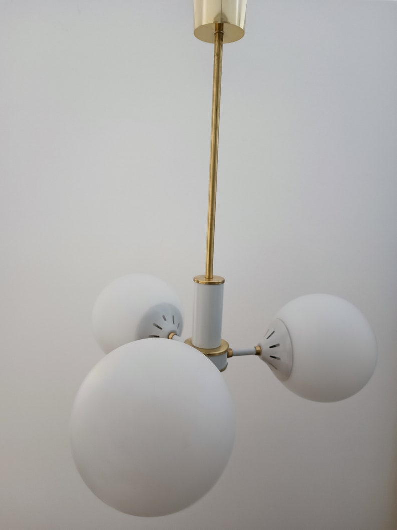 Peut inclure: Un plafonnier moderne avec trois abat-jours globulaires blancs. Le luminaire pr&eacute;sente une tige centrale et des accents dor&eacute;s, avec des d&eacute;tails blancs et dor&eacute;s. Les abat-jours sont espac&eacute;s uniform&eacute;ment, cr&eacute;ant un design &eacute;quilibr&eacute;.