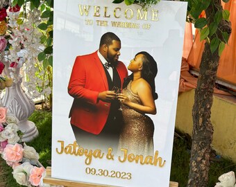 May include: A white welcome sign with a photo of a couple in red and gold attire. The sign reads "Welcome to the Wedding of Jatoya & Jonah" and the date "09.30.2023".