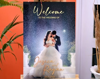 May include: A wedding welcome sign with a photo of a couple in the rain. The sign says "Welcome to the wedding of Jessica and Rayan 09.21.2023".