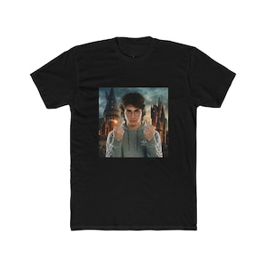 Può includere: T-shirt nero con grafica di una persona con occhiali e felpa grigia, che mostra il dito medio. Lo sfondo mostra un castello. La maglietta è un misto cotone.