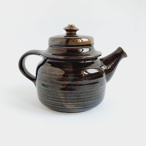 Könnte beinhalten: Eine braune Teekanne aus Keramik mit Deckel und Ausguss. Die Teekanne hat eine dunkelbraune Glasur mit einem dezenten Streifenmuster.
