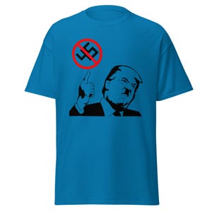 Könnte beinhalten: Ein blaues T-Shirt mit einem Schwarzweißbild einer Person mit einem roten Kreis und einem schwarzen Hakenkreuz mit einem diagonalen Strich durch. Der Text "Nein" ist in Rot im Kreis geschrieben.