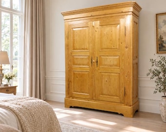 Pode incluir: Um guarda-roupa de madeira alto e retangular com acabamento natural em castanho claro e veios de madeira visíveis. A peça tem duas portas grandes, cada uma com dois painéis embutidos, e ferragens de metal escuro no centro.