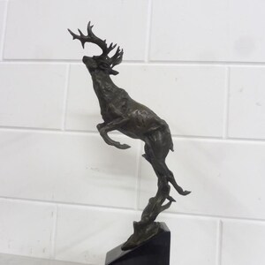 Könnte beinhalten: Eine Bronzeskulptur eines springenden Hirsches mit Geweih, die auf einem schwarzen Marmorsockel steht.
